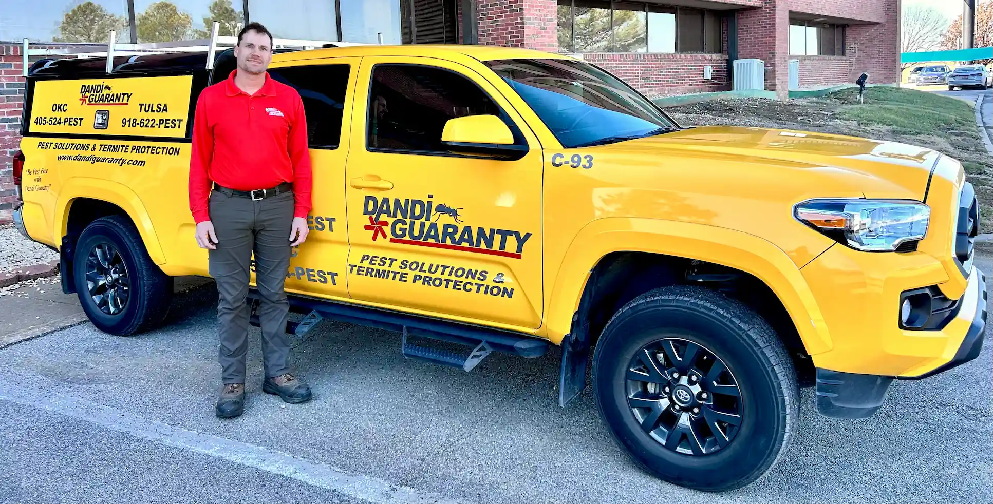 A Dandi Guaranty pest control technician standing next to a branded yellow service truck